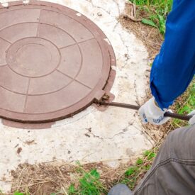 A,Plumber,Opens,A,Manhole,Cover,On,A,Concrete,Well